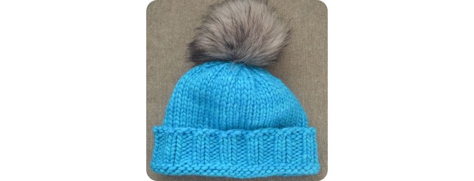 Strikket hue i Malabrigo Rasta garn i farven cian med en kæmpe pelskvast. Alle materialer fås hos strikmedhenni-shop.dk